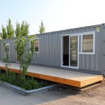 ตู้คอนเทนเนอร์เหล็กดัดแปลงเป็นออฟฟิศชั่วคราว พร้อมระเบียงไม้และต้นไม้ตกแต่งด้านหน้า